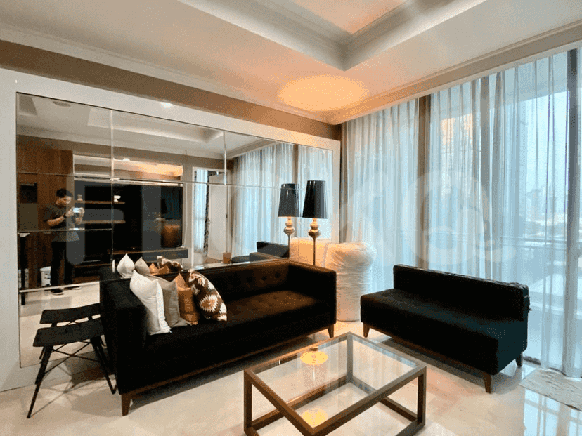A living room with a large mirror, dark sofas, and a glass coffee table.