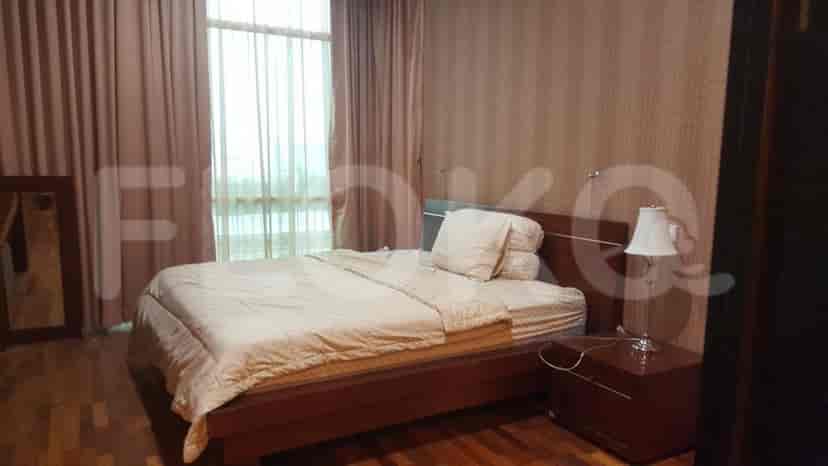 A well-lit bedroom with a king-sized bed, wooden floors, and large windows draped with curtains.