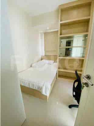 Kamar tidur kecil dengan tempat tidur single, rak built-in, dan kursi hitam.