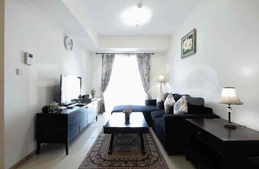 Ruang tamu yang luas dengan sofa hitam berbentuk L, TV yang dipasang di dinding, dan jendela besar dengan gorden.