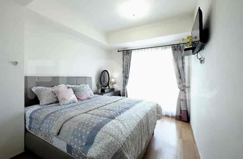 Kamar tidur dengan tempat tidur, bantal dekoratif, dan TV yang dipasang di dinding.