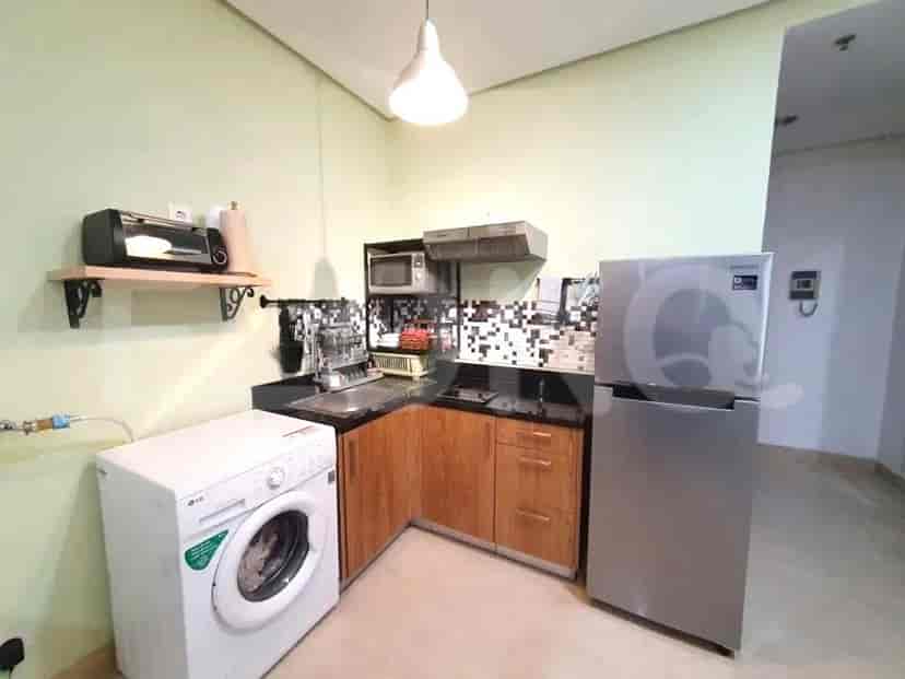 A compact kitchen with wooden cabinets, a stainless steel refrigerator, a washing machine, and a microwave.
