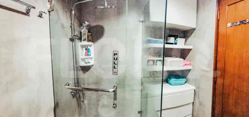 A modern bathroom with a glass shower enclosure, shelves, and a wooden door.