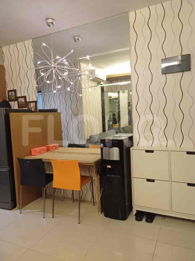 A dining area with a table, chairs, and lighting fixtures, with a kitchen in the background.