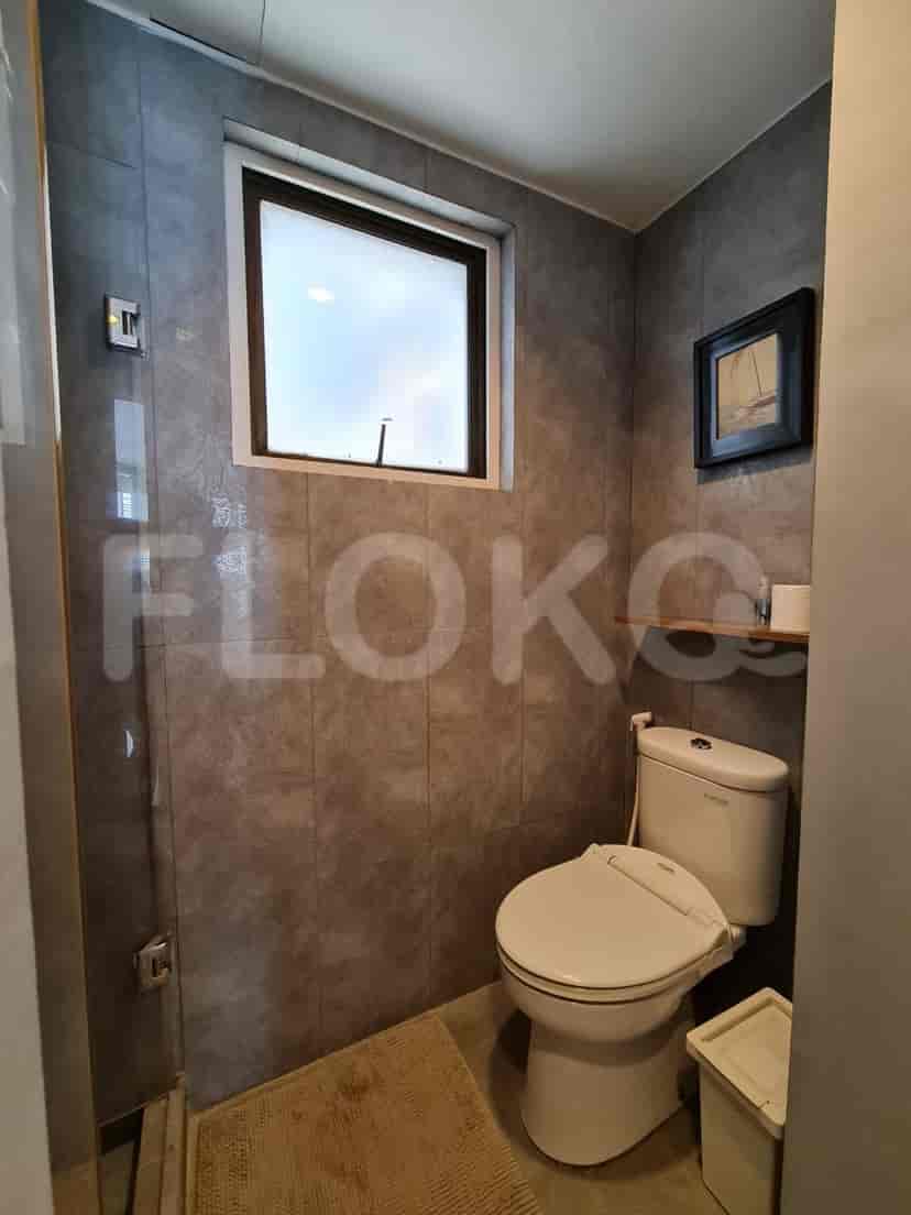 A bathroom with a toilet, a small window, and a tiled shower.