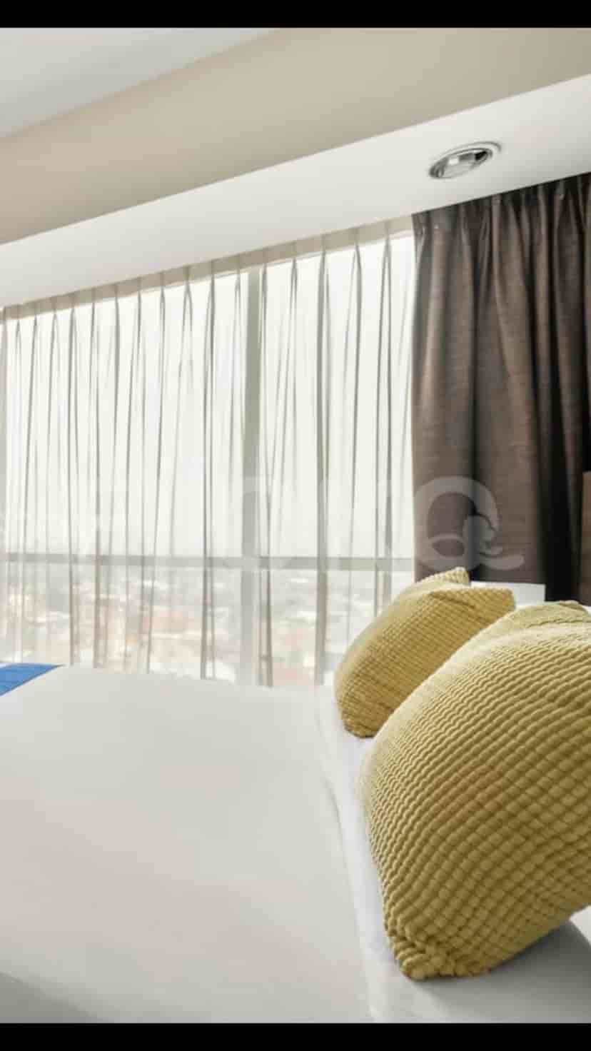 A bright bedroom with a large window and sheer curtains, offering a city view.