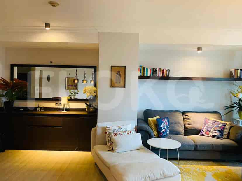Ruang tamu dengan chaise lounge berwarna terang dan sofa abu-abu; fitur termasuk lantai kayu dan tanaman.