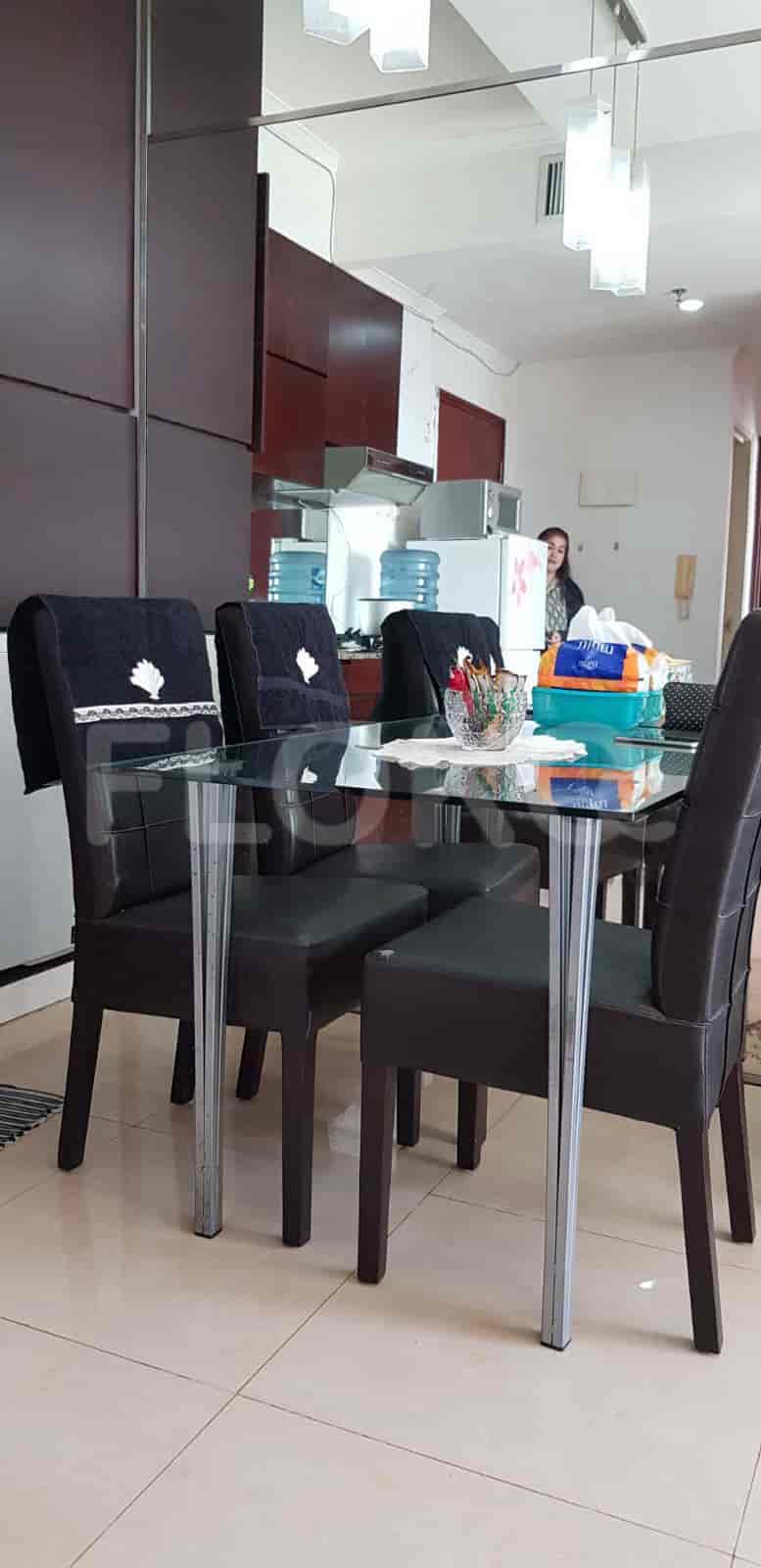 A dining room with a glass table and leather chairs, with a kitchen visible in the background.