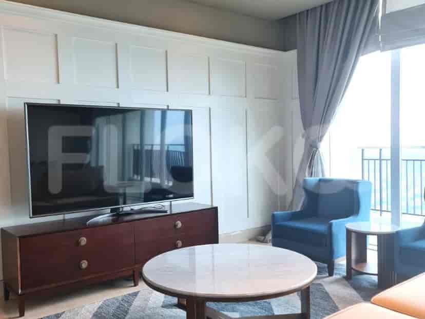 A living room with a TV, a cabinet, a round coffee table, and two blue armchairs.