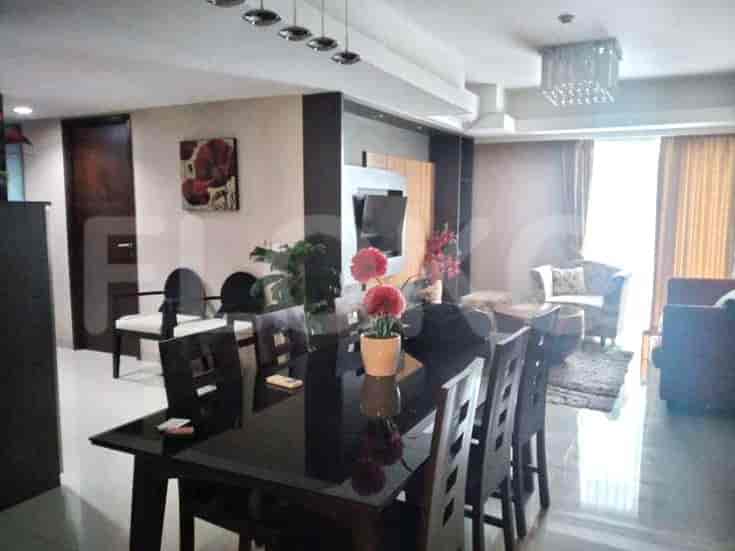 A dining area with a dark wood table and chairs, leading into a living room with a seating area and large windows.