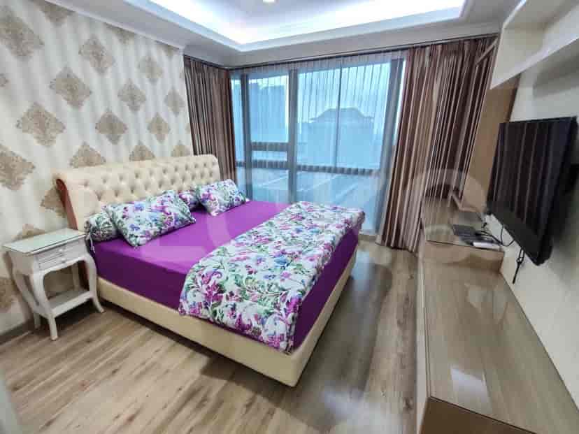 A stylish bedroom with a purple bed, large windows and wallpapered walls.
