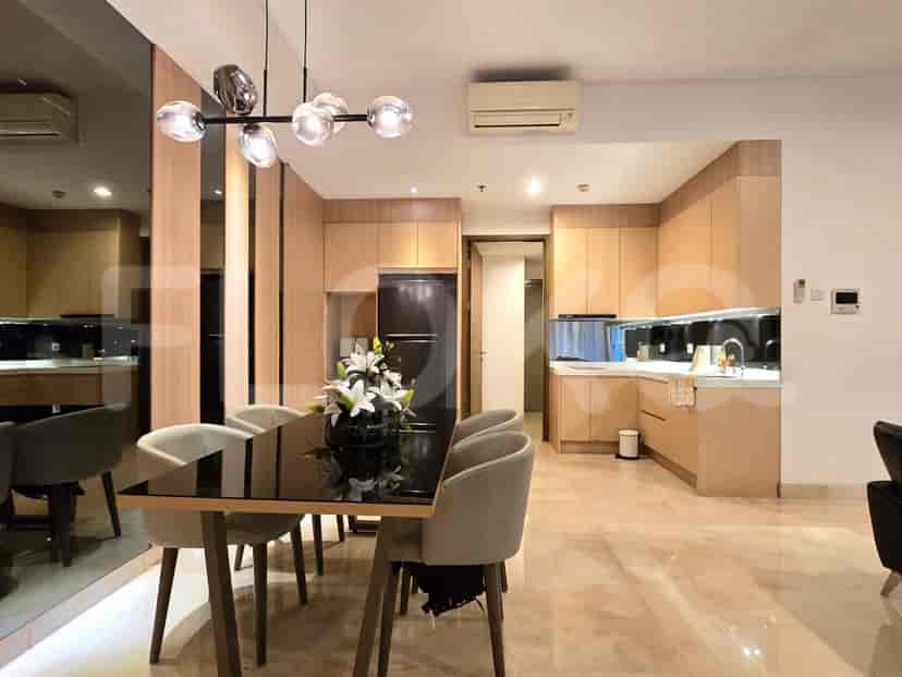 Area makan dan dapur terbuka yang menampilkan meja makan dengan kursi, lemari dapur kayu, dan lampu modern.