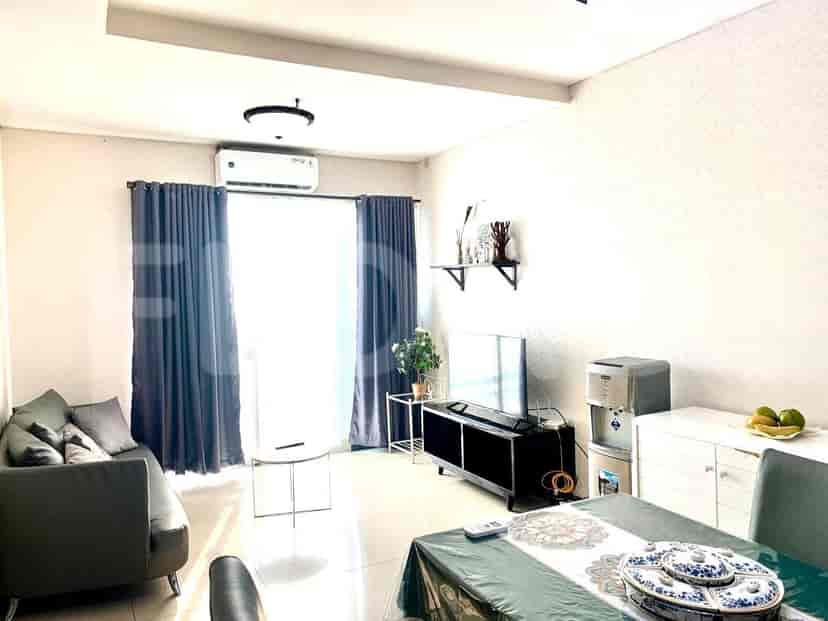 Ruang tamu yang terang benderang menampilkan sofa, TV, meja makan, dan jendela dengan gorden.