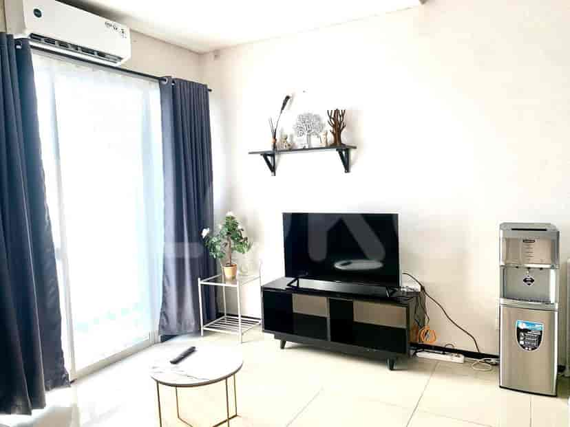 Pemandangan ruang tamu dengan TV, meja, dan jendela.