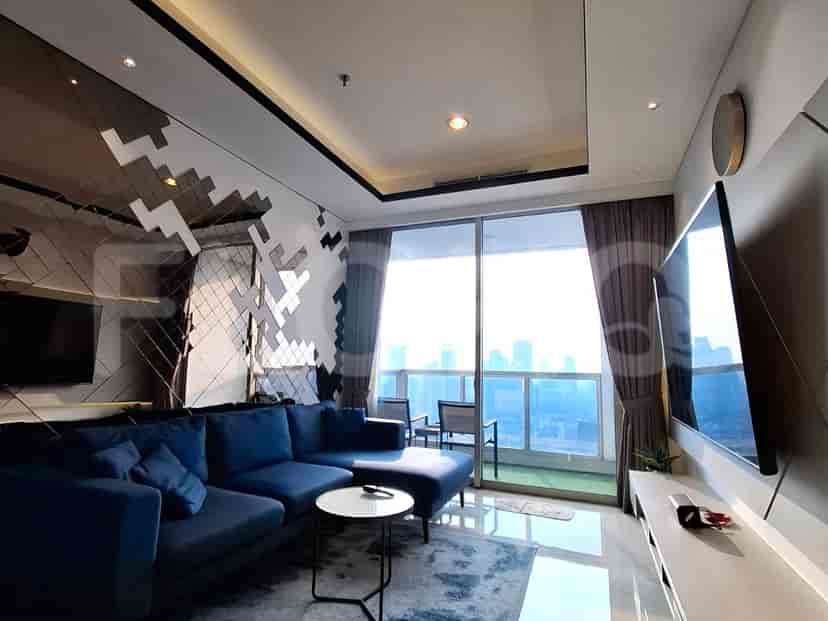Ruang tamu modern dengan sofa biru, TV yang dipasang di dinding, dan pemandangan kota.
