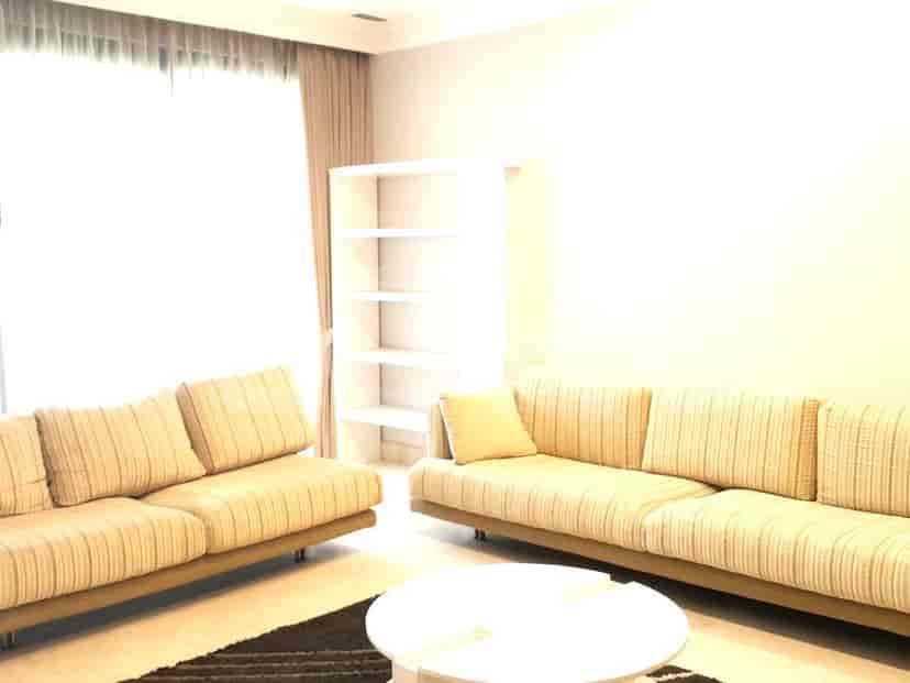 A bright living room with a neutral sofa, a white bookshelf, and a rug.