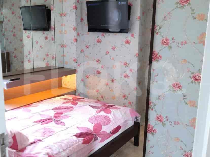 Small bedroom with bed, tv, mirror and floral wallpaper.