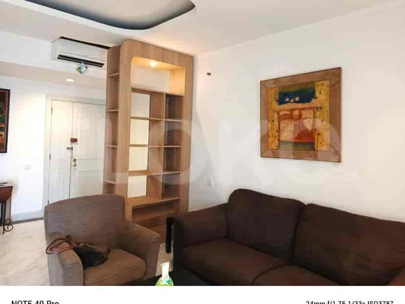 A living room with a brown sofa, wooden bookshelf, and artwork.