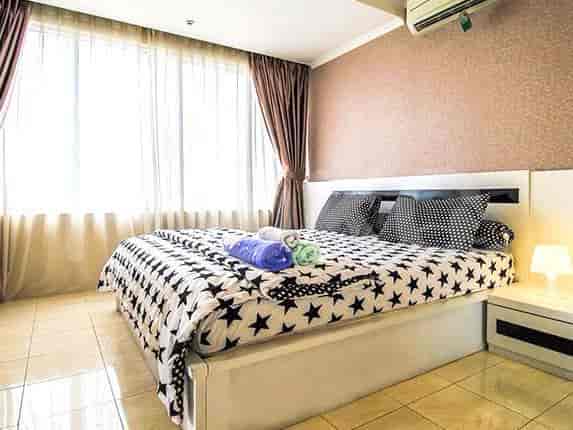 Kamar tidur modern dengan tempat tidur besar, meja samping, dan jendela besar.
