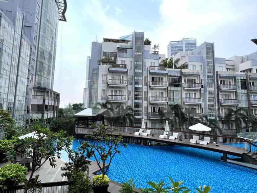 Outdoor swimming pool area with a bridge, lounge chairs, and surrounding buildings.