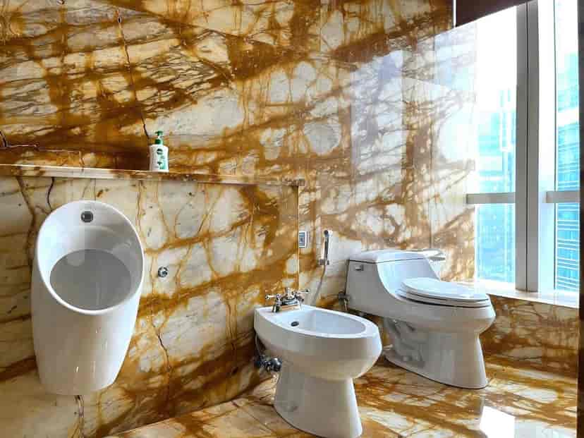 Kamar mandi mewah yang menampilkan urinal, bidet, dan toilet dengan dinding marmer.