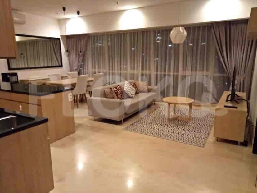 Living room with a sofa, TV, rug, and a kitchen area. A round wooden table and a beige rug add to the room's decor.