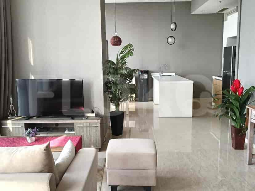 Living room with a view to the kitchen, featuring a TV, grey ottoman, and a dining space.