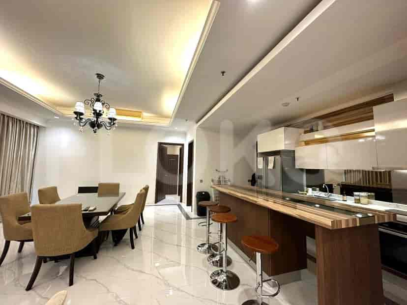 A dining area adjacent to a kitchen with a bar counter, featuring a chandelier and wooden stools.