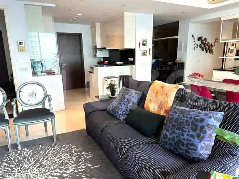 Ruang tamu dengan dapur dan ruang makan terbuka, menampilkan sofa, kursi, dan karpet bundar.