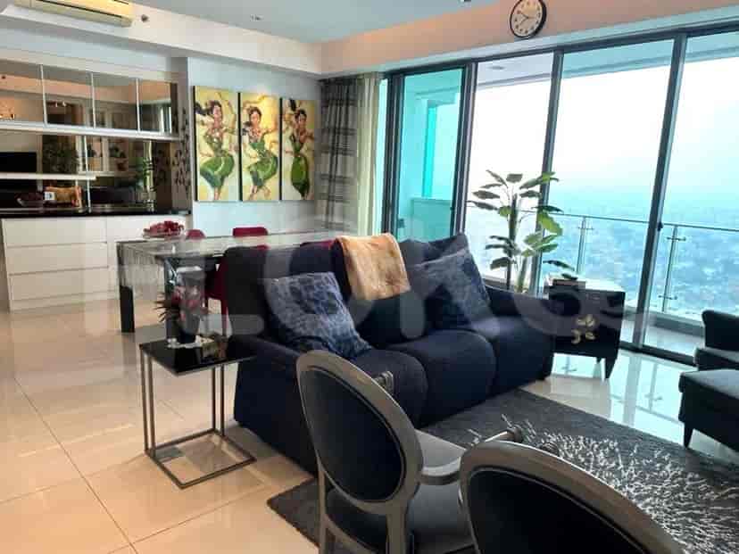 Ruang tamu modern dengan sofa biru tua, karya seni, dan jendela besar dengan pemandangan kota.