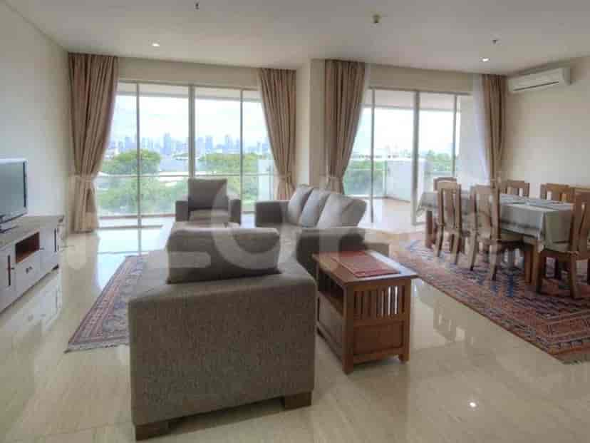 A spacious living room with an L-shaped grey sofa, wall-mounted smart TV, and large window with sheer curtains.