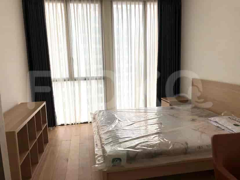 Kamar tidur dengan rangka tempat tidur kayu, tempat tidur dengan plastik pelindung, meja samping tempat tidur, gorden dan lantai kayu.
