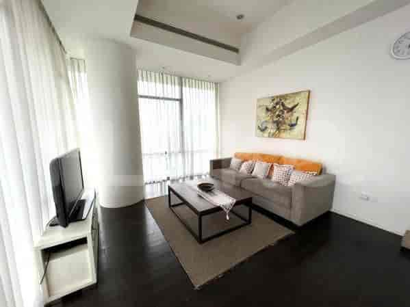 A spacious living room with an L-shaped grey sofa, wall-mounted smart TV, and large window with sheer curtains.