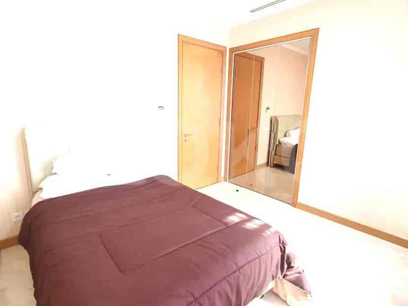 Kamar tidur modern dengan tempat tidur, pintu lemari cermin, dan warna netral.