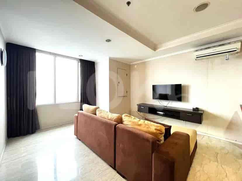 Ruang tamu dengan sofa cokelat, TV, dan jendela besar dengan gorden gelap.