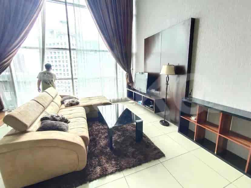 Ruang tamu modern dengan sofa berbentuk L, jendela besar, dan konsol TV.