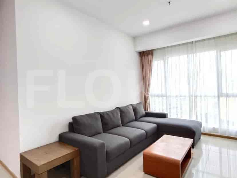 A modern living room with a grey L-shaped sofa, wooden side table, and large windows.