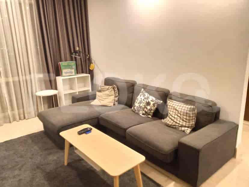 A spacious living room with an L-shaped grey sofa, wall-mounted smart TV, and large window with sheer curtains.