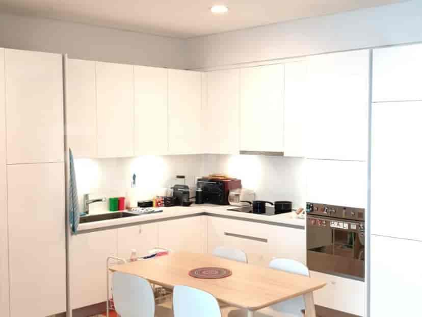 A modern kitchen with white cabinets, wooden table, and appliances.