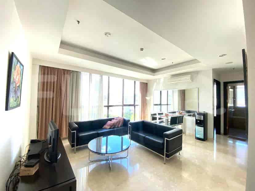 A living room featuring black leather sofas, a round glass coffee table, and a dining area visible in the background.