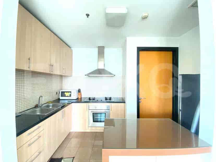 A modern kitchen with light wood cabinets, a stainless steel range hood, and a black countertop.