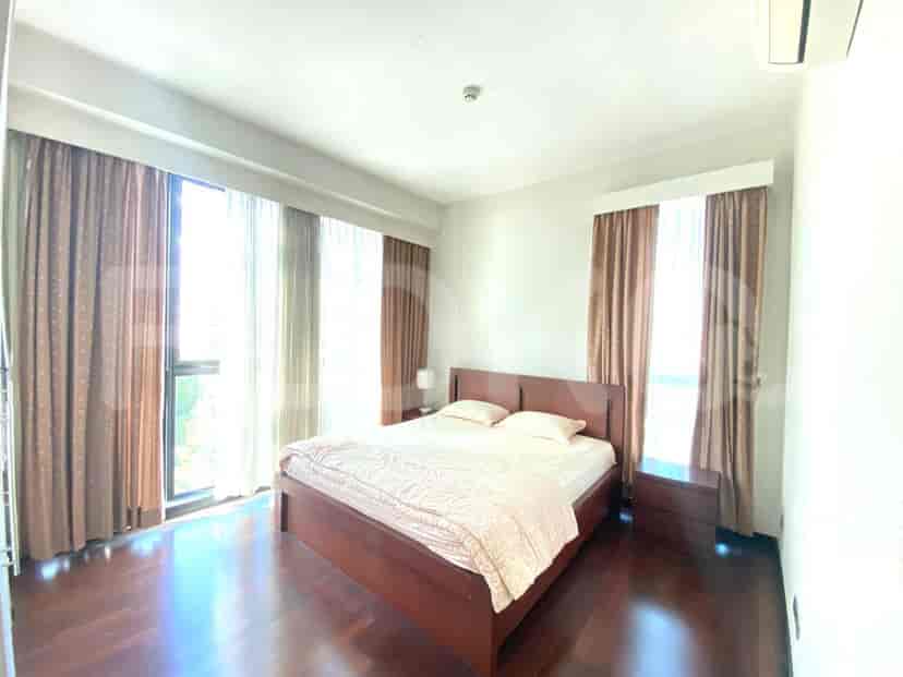 A bedroom featuring a double bed, wooden flooring, and large windows with brown curtains.