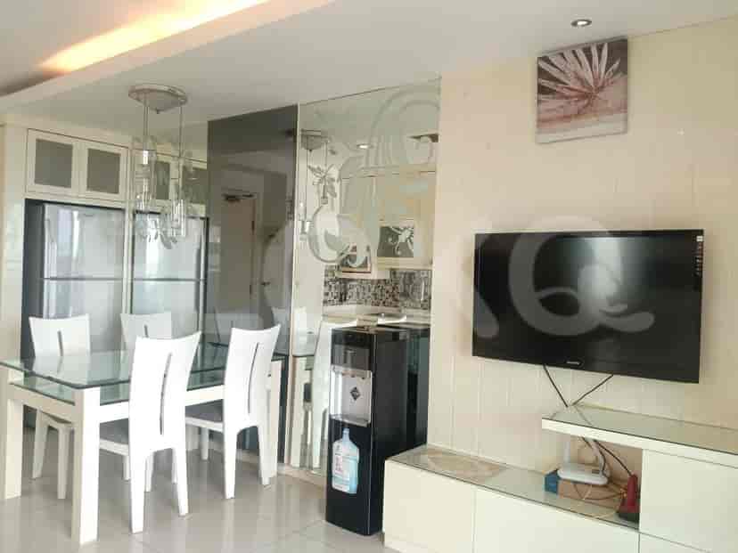 A dining area with a glass-topped table and white chairs adjacent to a living space with a mounted TV.