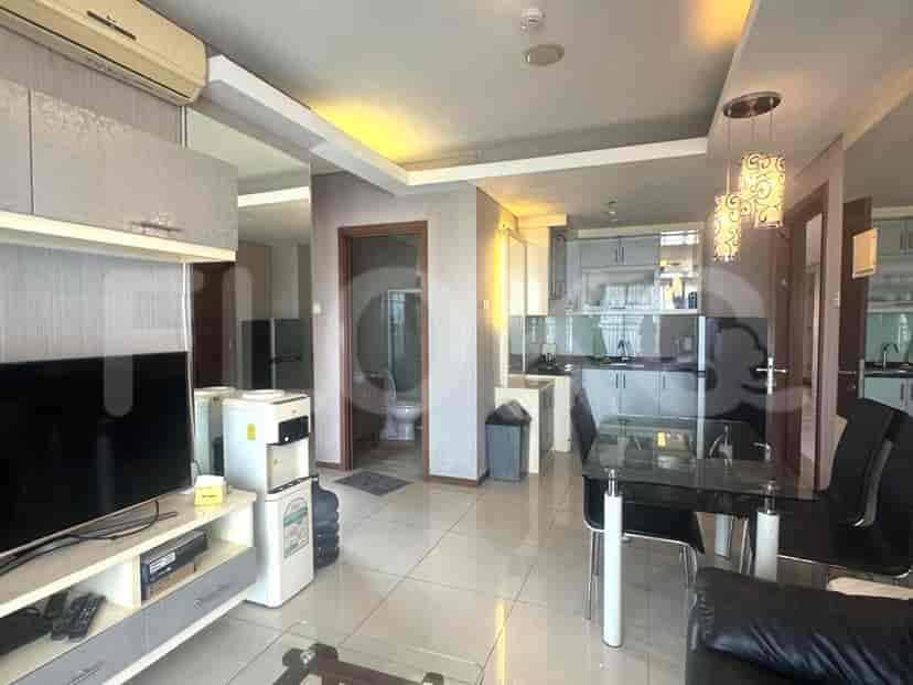 Ruang tamu yang terang dengan TV, akses dapur, dan ruang makan.