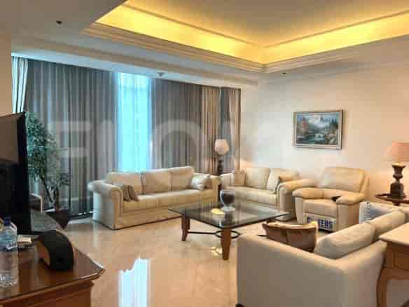Ruang tamu yang luas dengan beberapa sofa berwarna krem, meja kopi kaca, dan jendela besar dengan gorden tipis.