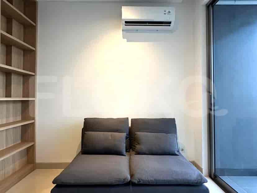 A modern living area featuring a gray futon-style sofa, air conditioning, and a wooden bookshelf.