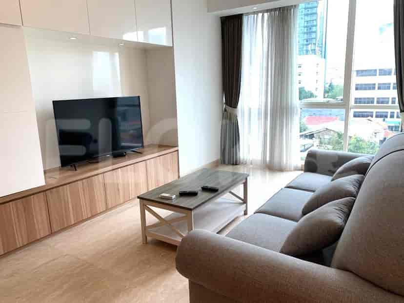 Ruang tamu dengan sofa abu-abu, meja kopi kayu, TV, dan jendela besar.