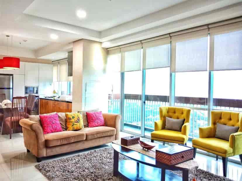 A well-lit living room with a brown sofa, yellow armchairs, and large windows overlooking a city view.