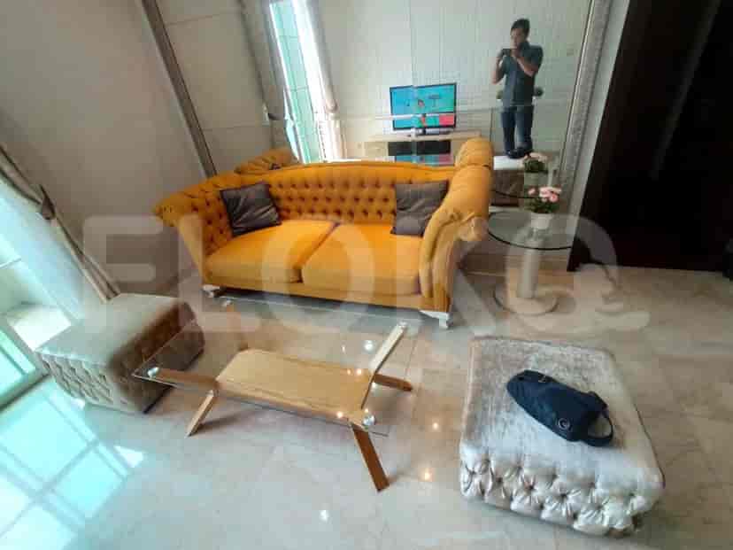A living room with an orange sofa, glass coffee table, and ottomans.