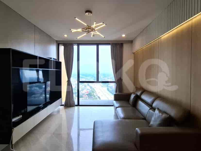 Ruang tamu modern dengan sofa berbentuk L berwarna abu-abu, TV yang dipasang di dinding, dan jendela besar yang menawarkan pemandangan kota.